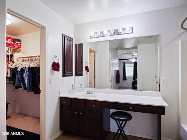 full bathroom featuring baseboards, vanity, a walk in closet, and ceiling fan