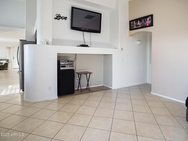 unfurnished living room featuring arched walkways, light tile patterned floors, and a high ceiling