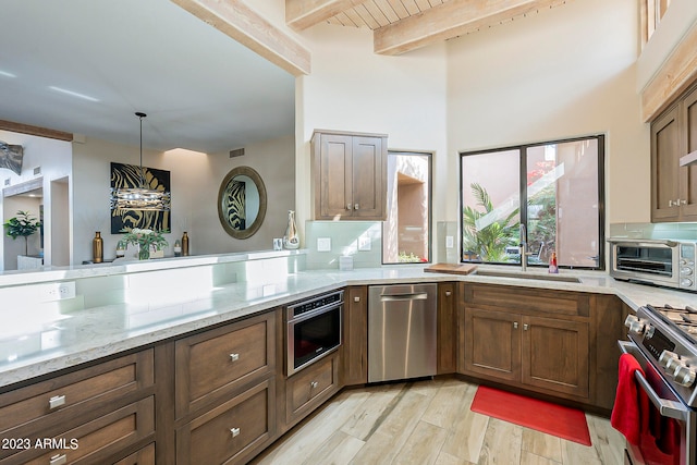 kitchen with sink, light wood-type flooring, hanging light fixtures, stainless steel appliances, and beam ceiling