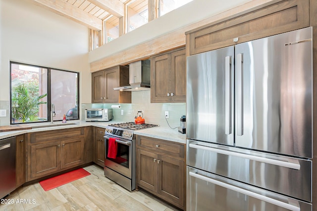 kitchen with decorative backsplash, light hardwood / wood-style flooring, sink, wall chimney exhaust hood, and stainless steel appliances