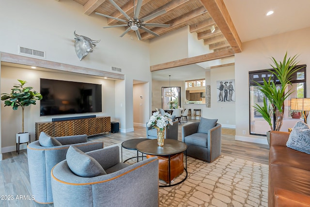 living room with a towering ceiling, light hardwood / wood-style floors, ceiling fan, beamed ceiling, and wooden ceiling