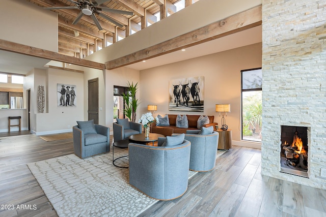 living room featuring beam ceiling, a stone fireplace, a towering ceiling, and hardwood / wood-style floors