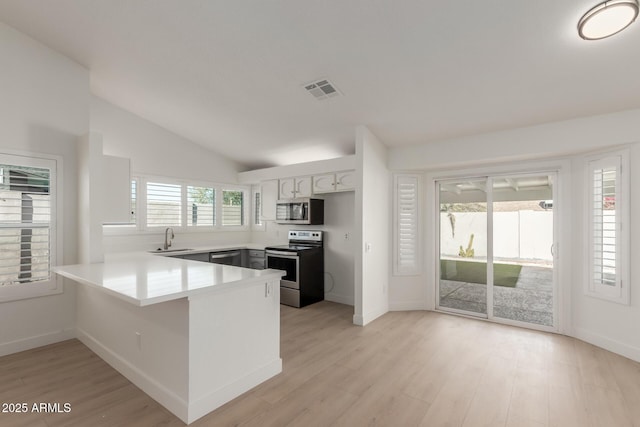 kitchen with lofted ceiling, kitchen peninsula, sink, white cabinetry, and stainless steel appliances