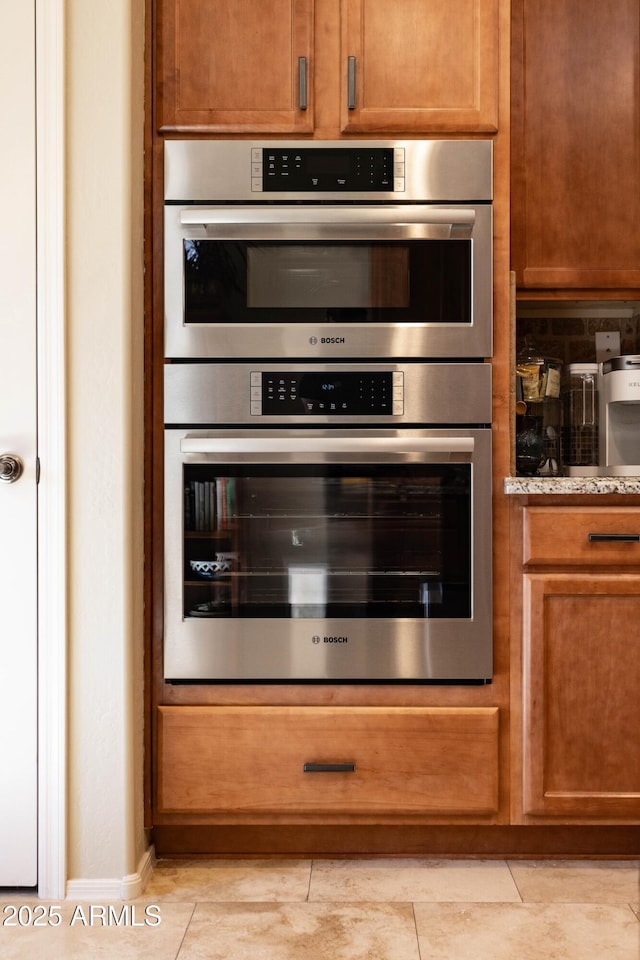 kitchen featuring light stone countertops, light tile patterned floors, and stainless steel double oven