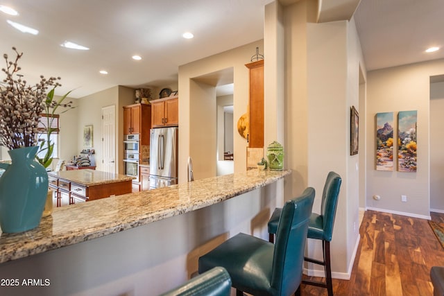 kitchen featuring kitchen peninsula, light stone countertops, dark wood-type flooring, and appliances with stainless steel finishes