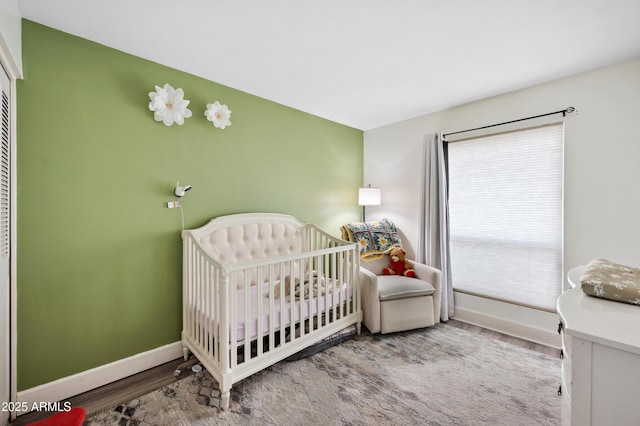 bedroom with a crib, wood finished floors, and baseboards