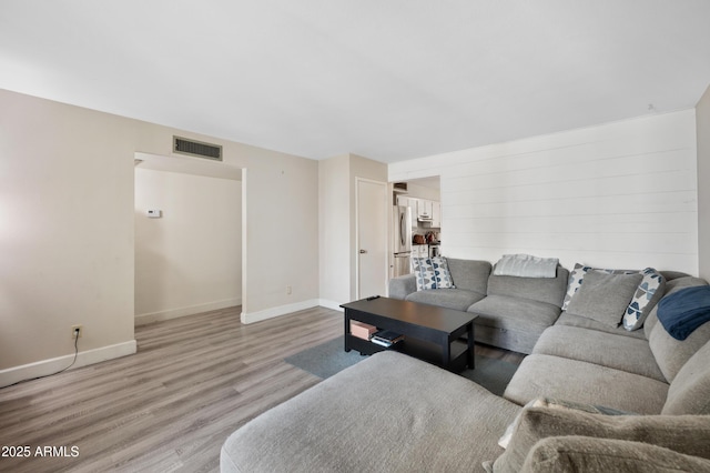 living room featuring visible vents, light wood-style flooring, and baseboards