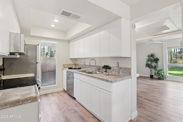 kitchen featuring dishwasher, sink, white cabinets, a tray ceiling, and light wood-type flooring