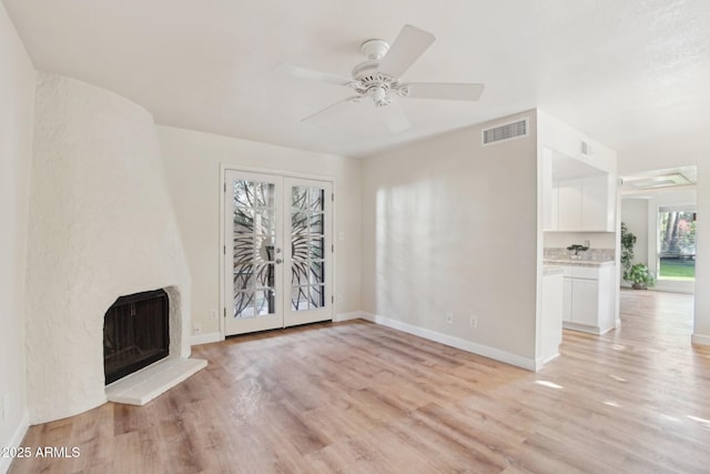 unfurnished living room with light wood-type flooring, french doors, a large fireplace, and ceiling fan