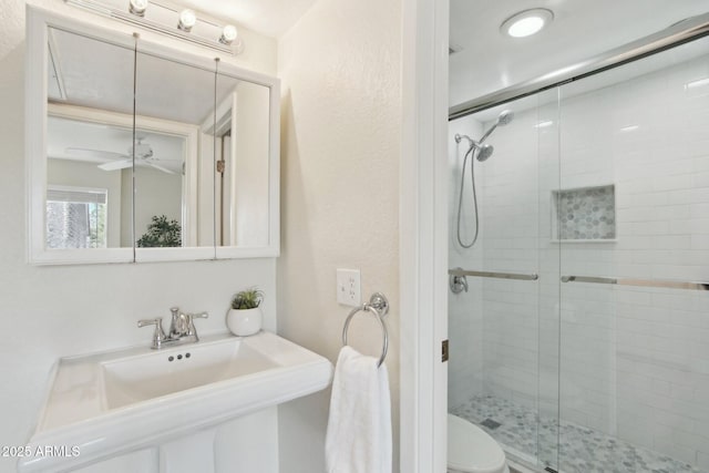 bathroom featuring toilet, ceiling fan, an enclosed shower, and sink