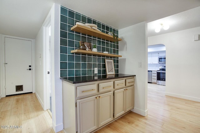 kitchen featuring light wood-style flooring, tasteful backsplash, arched walkways, appliances with stainless steel finishes, and cream cabinets
