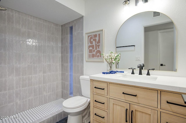bathroom featuring visible vents, toilet, a tile shower, and vanity