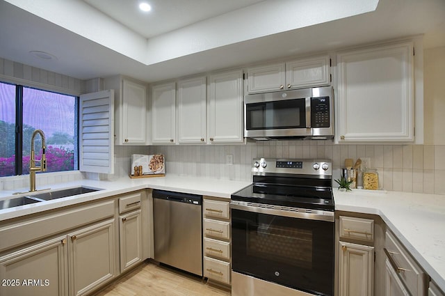 kitchen with light countertops, a sink, light wood-type flooring, stainless steel appliances, and decorative backsplash