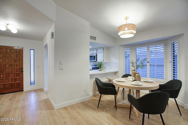 dining space featuring light wood-style flooring, a textured ceiling, baseboards, and visible vents