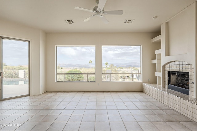 unfurnished living room featuring light tile patterned flooring, visible vents, a fireplace with raised hearth, and a healthy amount of sunlight