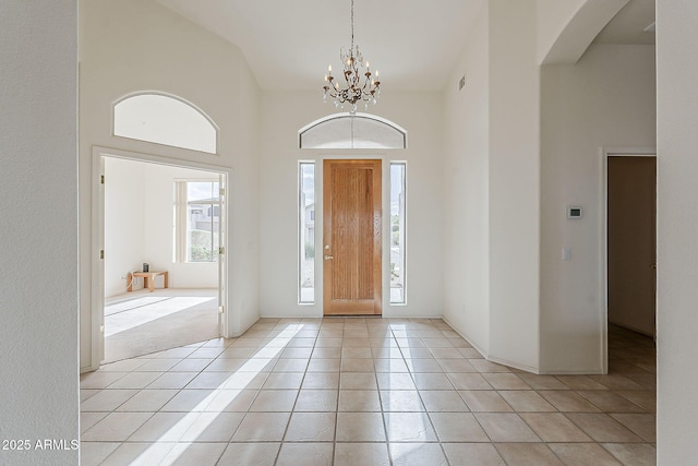 entryway featuring an inviting chandelier, a high ceiling, light tile patterned flooring, and arched walkways