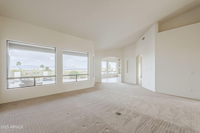 spare room featuring visible vents, light colored carpet, arched walkways, and high vaulted ceiling