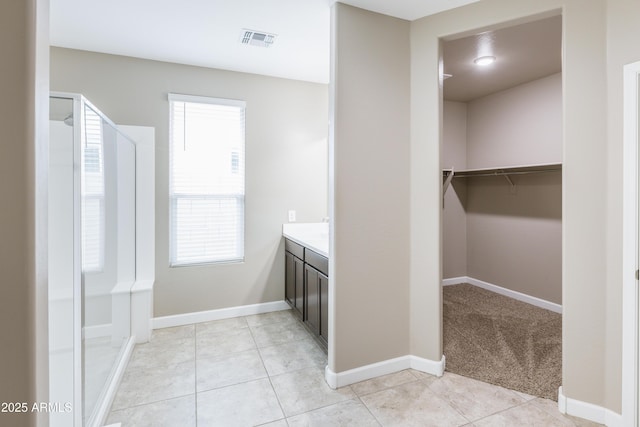 full bath featuring tile patterned floors, vanity, a walk in closet, baseboards, and visible vents