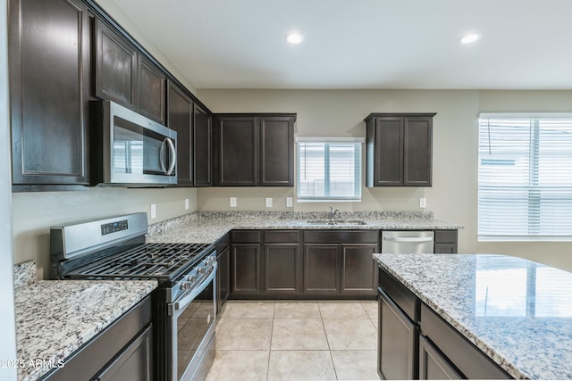 kitchen with recessed lighting, a sink, light stone counters, dark brown cabinetry, and appliances with stainless steel finishes