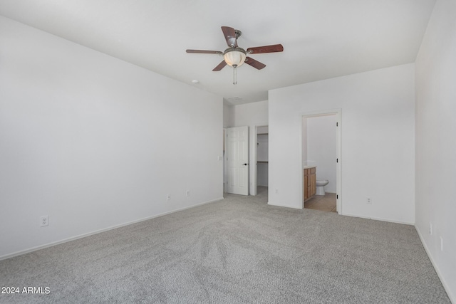 unfurnished bedroom featuring a walk in closet, ensuite bathroom, light carpet, ceiling fan, and baseboards