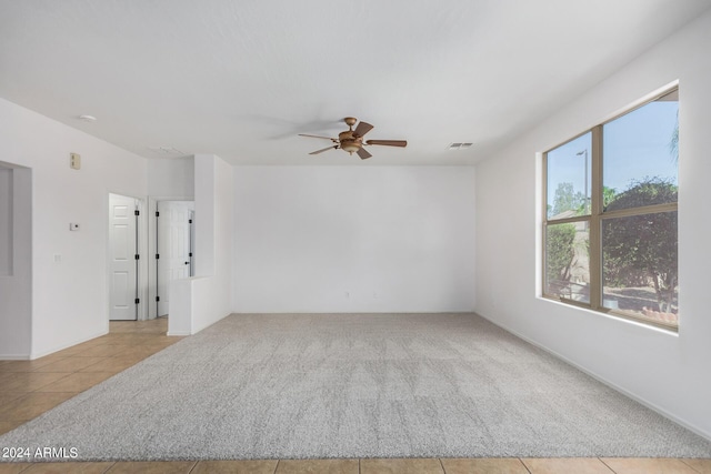 carpeted empty room with visible vents, a ceiling fan, and tile patterned floors