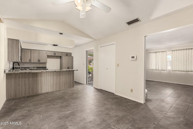 kitchen with healthy amount of natural light, ceiling fan, a peninsula, lofted ceiling, and light stone countertops