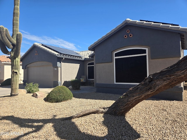 view of front of house with a garage, a tiled roof, roof mounted solar panels, and stucco siding