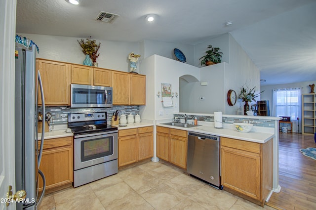 kitchen featuring sink, a textured ceiling, appliances with stainless steel finishes, tasteful backsplash, and kitchen peninsula