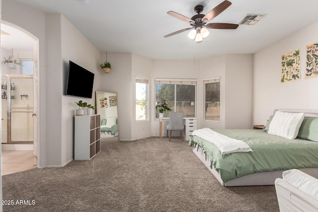 carpeted bedroom featuring visible vents, arched walkways, a ceiling fan, ensuite bath, and tile patterned flooring