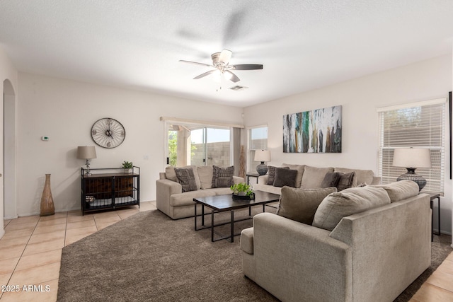 living room with visible vents, arched walkways, a ceiling fan, a textured ceiling, and light tile patterned flooring