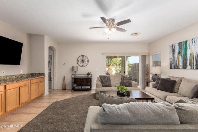 living room with light tile patterned floors, visible vents, arched walkways, and a ceiling fan