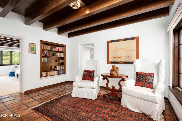 sitting room with dark tile patterned flooring, built in shelves, and beam ceiling