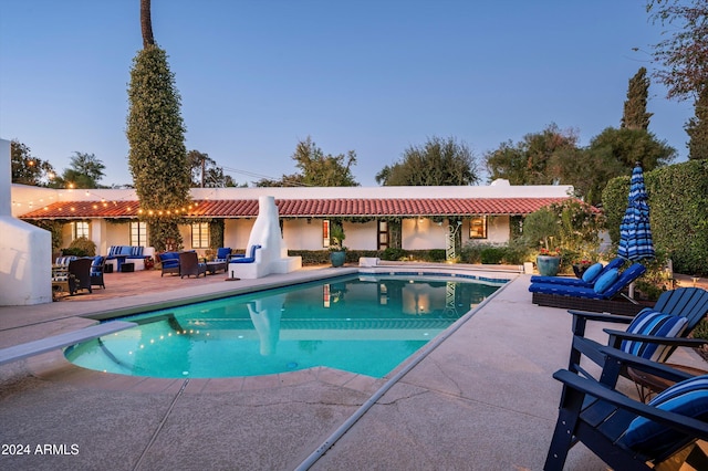 pool at dusk featuring a diving board, outdoor lounge area, and a patio