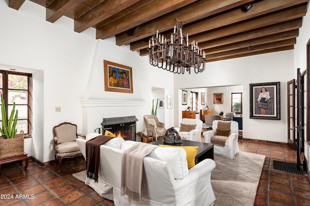 living room featuring plenty of natural light, beamed ceiling, dark tile patterned flooring, and a notable chandelier