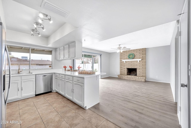 kitchen featuring kitchen peninsula, light wood-type flooring, a brick fireplace, stainless steel appliances, and white cabinetry