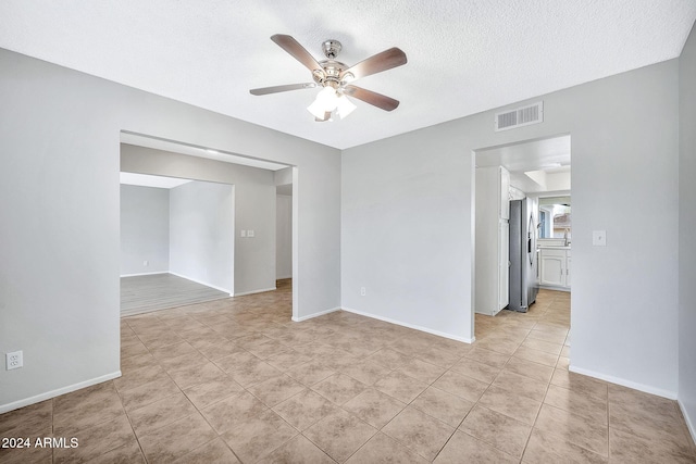 spare room featuring a textured ceiling, ceiling fan, and light tile patterned flooring