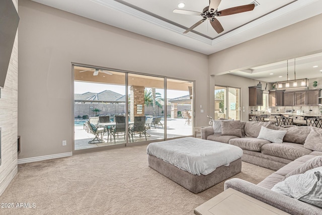 carpeted living room with ceiling fan, ornamental molding, a towering ceiling, and a tray ceiling