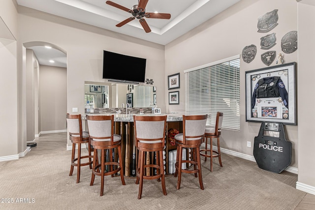 bar featuring light carpet, a tray ceiling, and ceiling fan