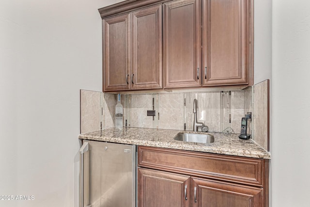 bar with decorative backsplash, light stone counters, and sink