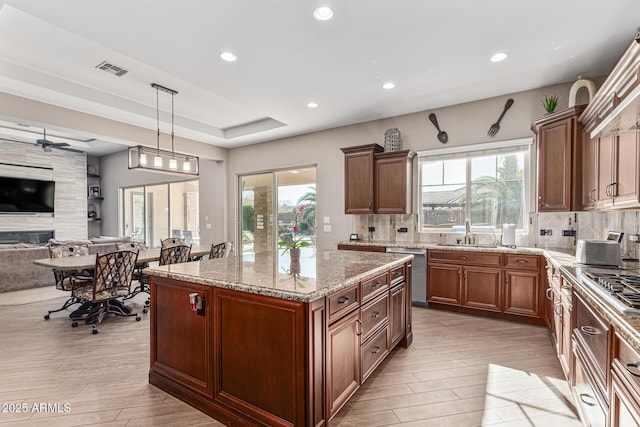 kitchen with a wealth of natural light, a raised ceiling, ceiling fan, decorative light fixtures, and a kitchen island