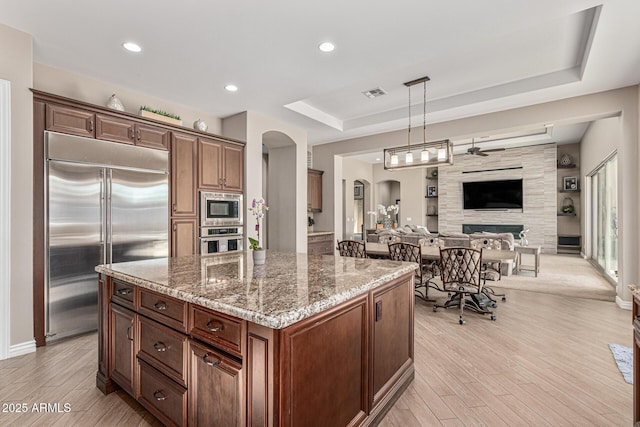 kitchen featuring built in appliances, dark stone counters, decorative light fixtures, a kitchen island, and light wood-type flooring