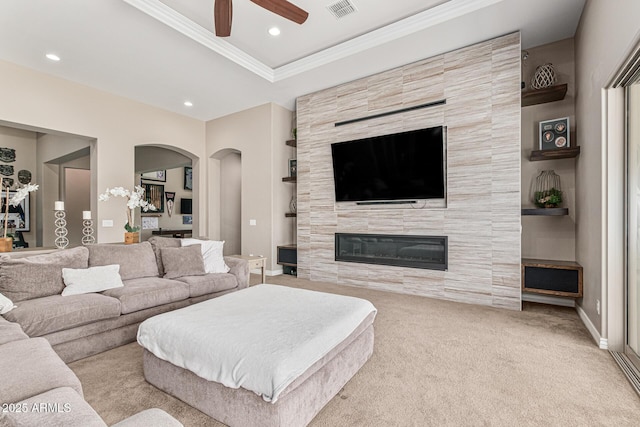 carpeted living room with ceiling fan, a fireplace, and ornamental molding