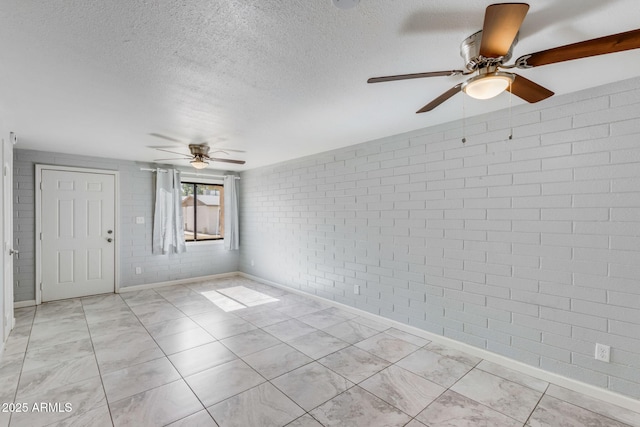 unfurnished room with baseboards, a textured ceiling, brick wall, and a ceiling fan