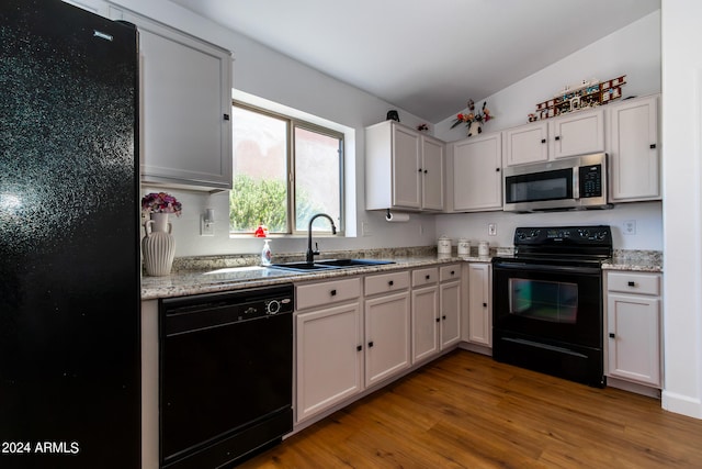 kitchen with white cabinetry, black appliances, sink, light stone countertops, and hardwood / wood-style flooring