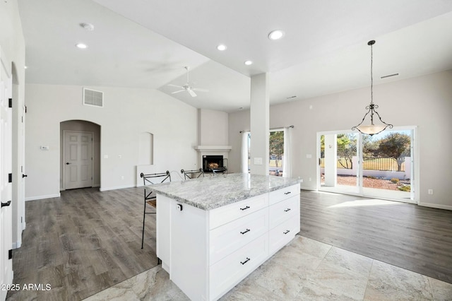 kitchen featuring white cabinets, a kitchen breakfast bar, hanging light fixtures, a fireplace, and a kitchen island