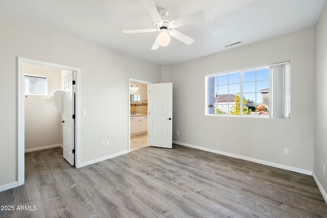 unfurnished bedroom featuring a walk in closet, ensuite bathroom, a closet, and light hardwood / wood-style floors