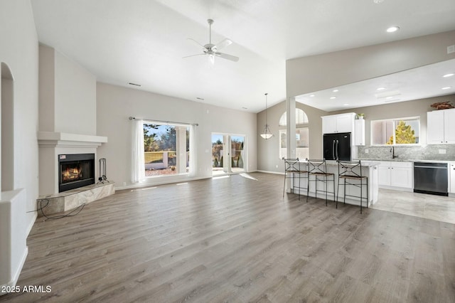 unfurnished living room featuring ceiling fan, sink, a high end fireplace, high vaulted ceiling, and light wood-type flooring