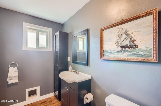 half bath featuring toilet, vanity, wood finished floors, and baseboards