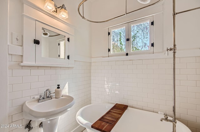 bathroom with tile walls, a freestanding tub, a sink, and tasteful backsplash