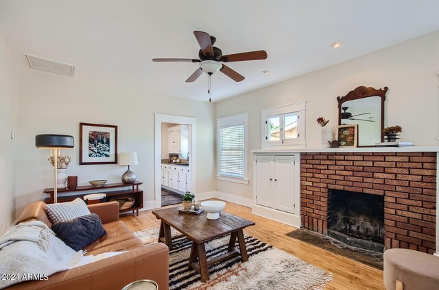 living area featuring ceiling fan, a fireplace, light wood-style flooring, and baseboards